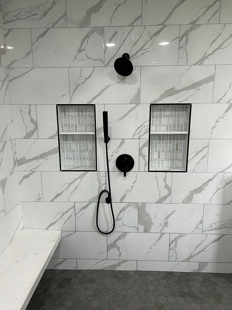 Siding, bathroom, garage & 1/2 bath — after: shower detail with marble-look tile, dual built-in niches, and black fixtures — Attica, Ohio
