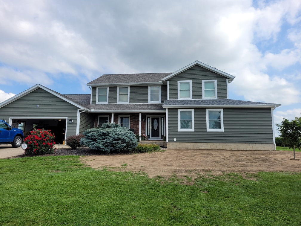 Siding, bathroom, garage & 1/2 bath — after: completed front exterior with new gray siding, brick accents, and covered porch — Attica, Ohio