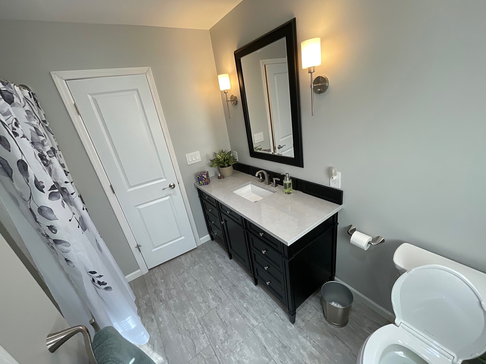 Bathroom remodel — after: new black vanity with quartz countertop, framed mirror, and wall sconces — Findlay, Ohio