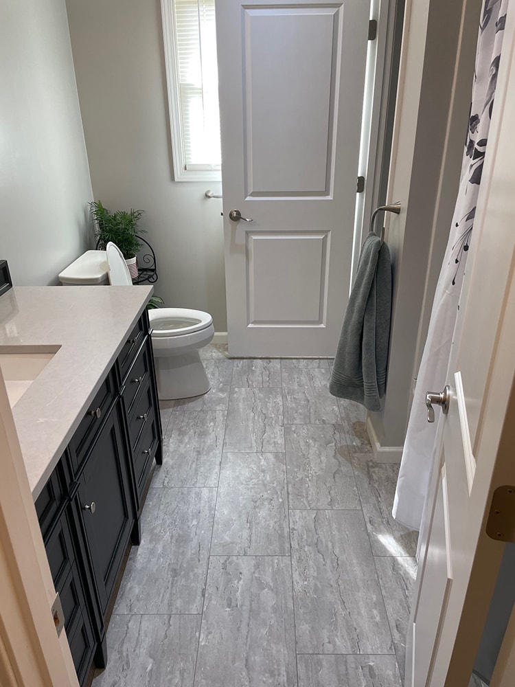 Bathroom remodel — after: full bathroom view with new gray tile floor, black vanity, and updated toilet — Findlay, Ohio