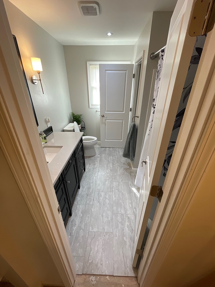 Bathroom remodel — after: doorway view of completed bathroom with new tile floor, vanity, and wall sconce — Findlay, Ohio
