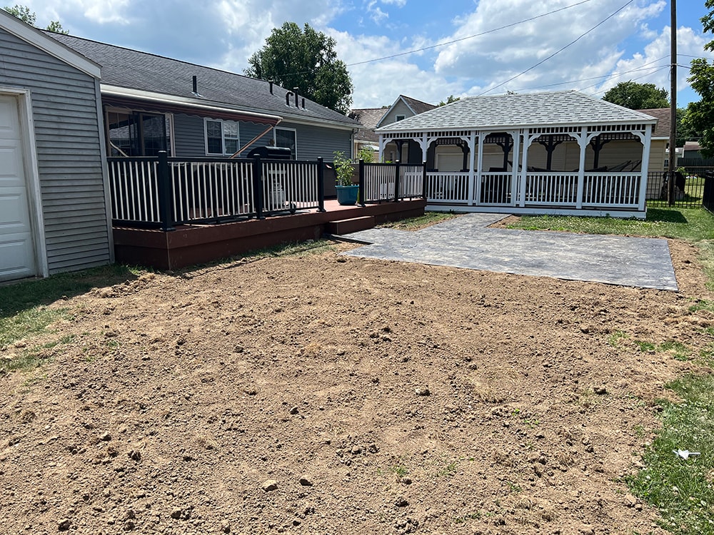 Composite deck — after: completed composite deck with black aluminum railing, steps, and stamped concrete patio below, wide backyard view, Findlay, Ohio
