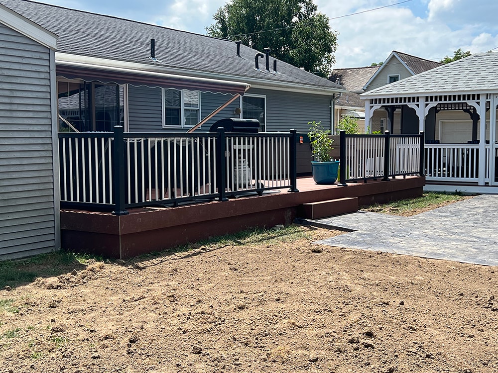 Composite deck — after: completed composite deck with black aluminum railing and steps, close rear view with stamped concrete patio, Findlay, Ohio