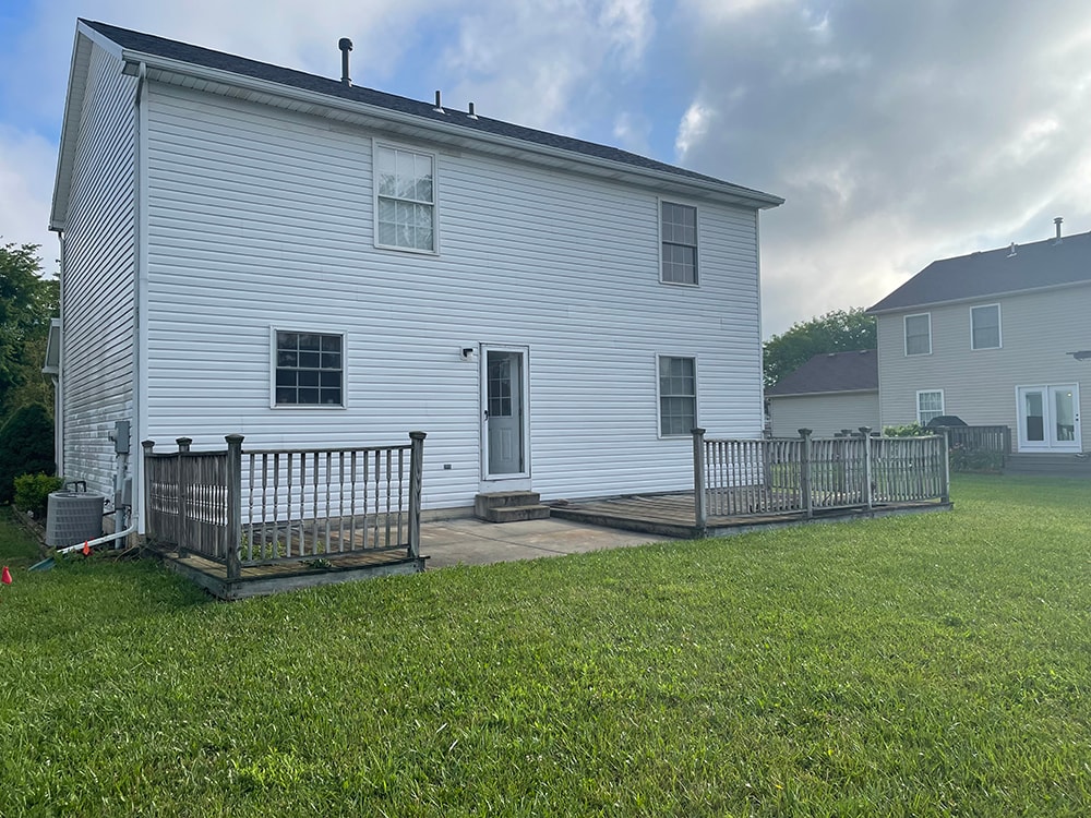 Deck addition — before: original weathered deck from opposite angle showing concrete patio and AC unit alongside two-story home, Findlay, Ohio