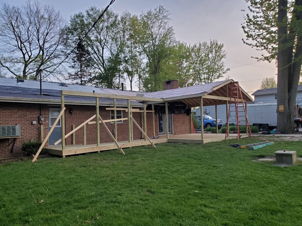 Deck addition Findlay — during: full deck platform framed with treated lumber and gable roof structure rising at dusk, red ladder visible, Findlay, Ohio