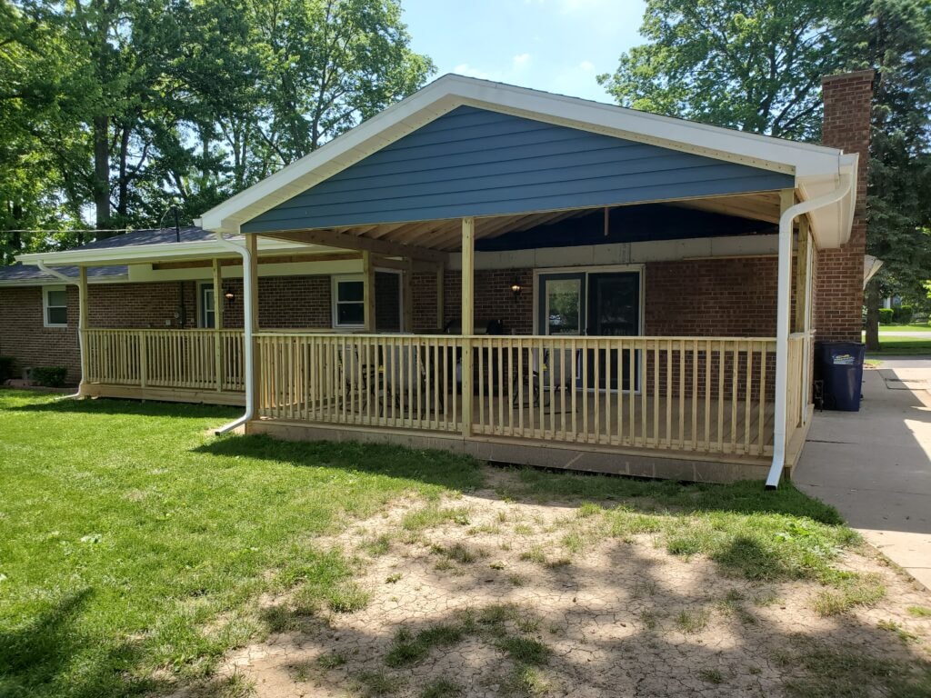 Deck addition Findlay — after: sunny wide shot of completed deck showing full treated railing, blue vinyl siding on gable end, and screened section with white gutters, Findlay, Ohio