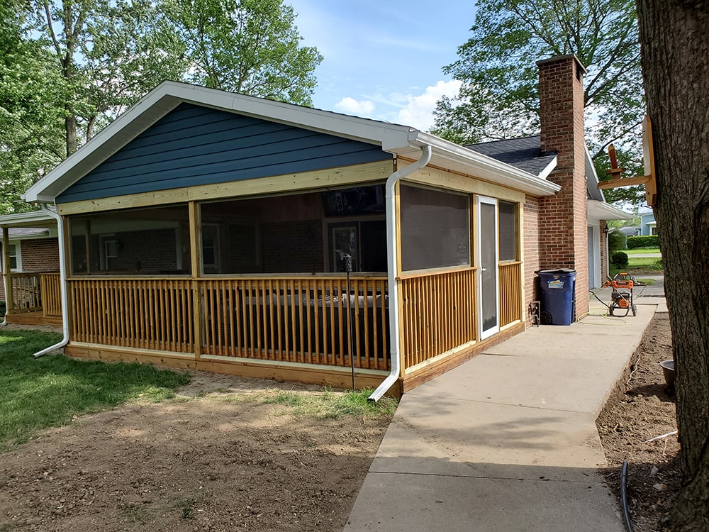 Deck addition Findlay — after: close-up of screened section corner showing blue vinyl siding gable, white fascia, white gutters, and treated wood railing, Findlay, Ohio