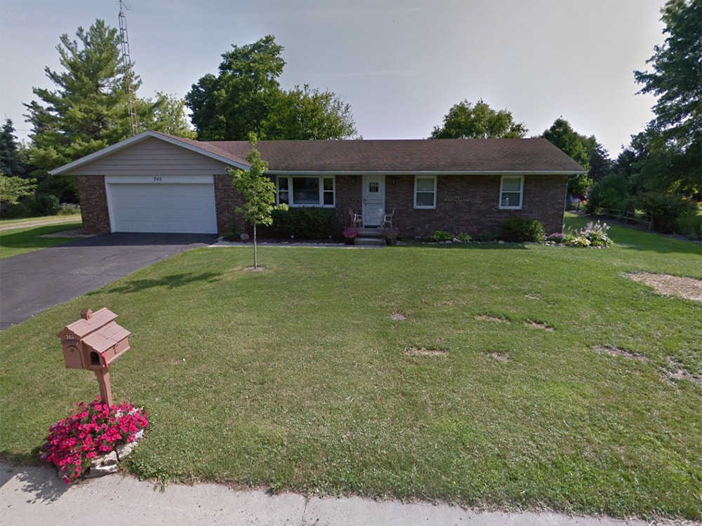 Composite deck with gable roof — before: original brick ranch home front view with mailbox and flower bed — Bluffton, Ohio