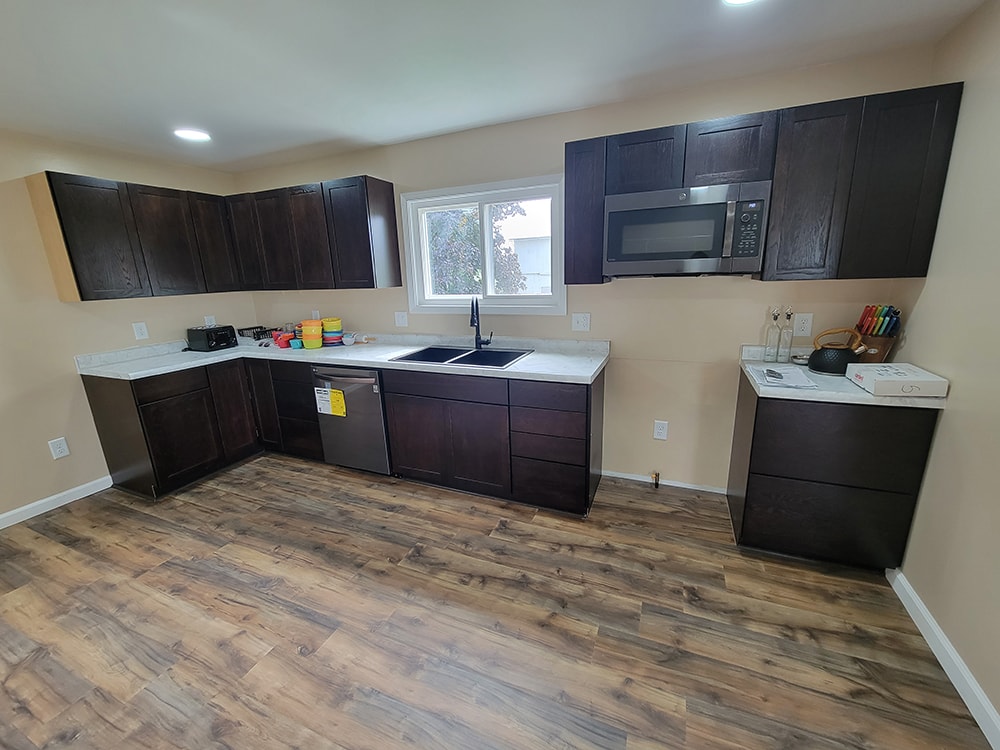 Entire house remodel — after: completed kitchen with dark cabinets, white countertops, and wood flooring — Arlington, Ohio