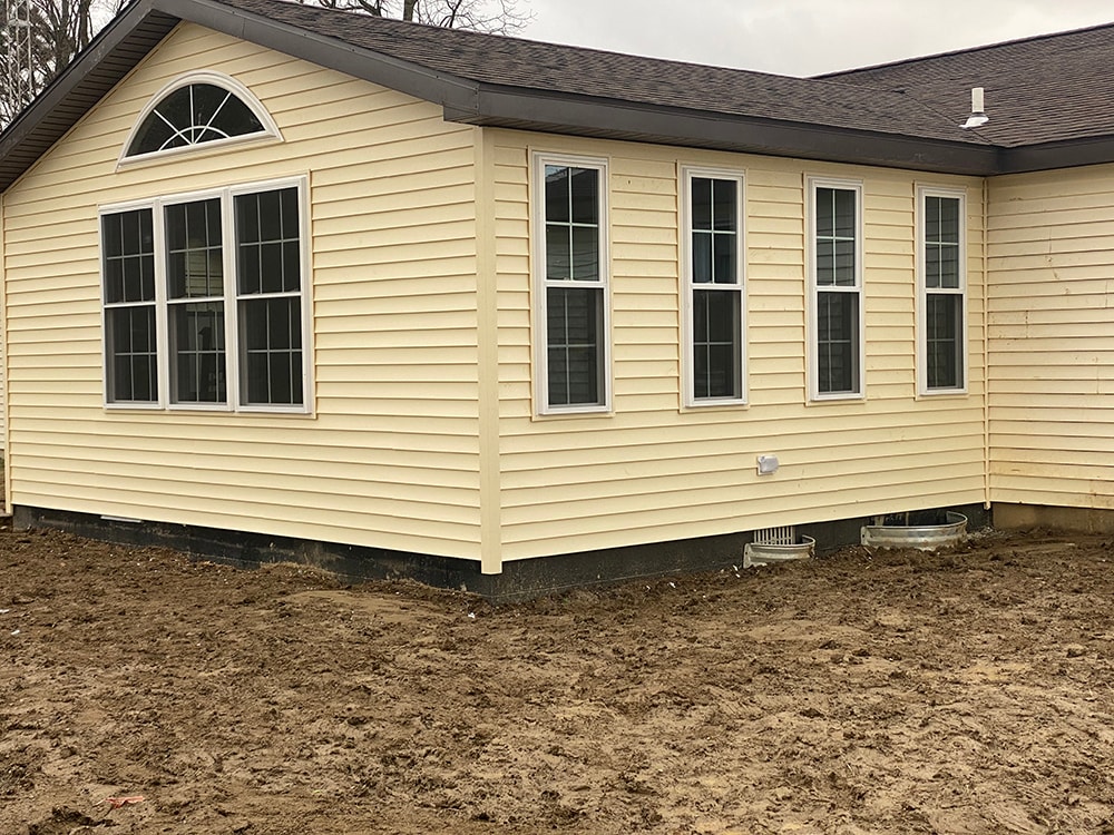 Room addition Fostoria — completed exterior side view with new cream vinyl siding, multiple double-hung windows, and dark trim, Fostoria, Ohio