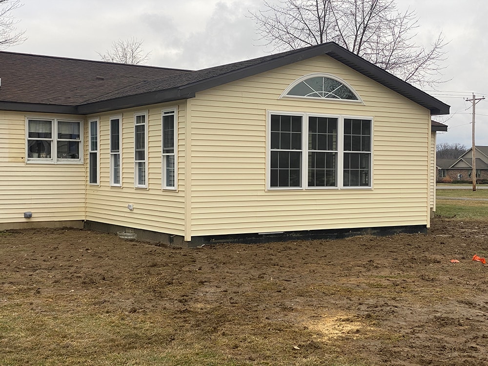 Room addition Fostoria — completed exterior angled view showing addition tying into existing home with matching cream siding and dark trim, Fostoria, Ohio