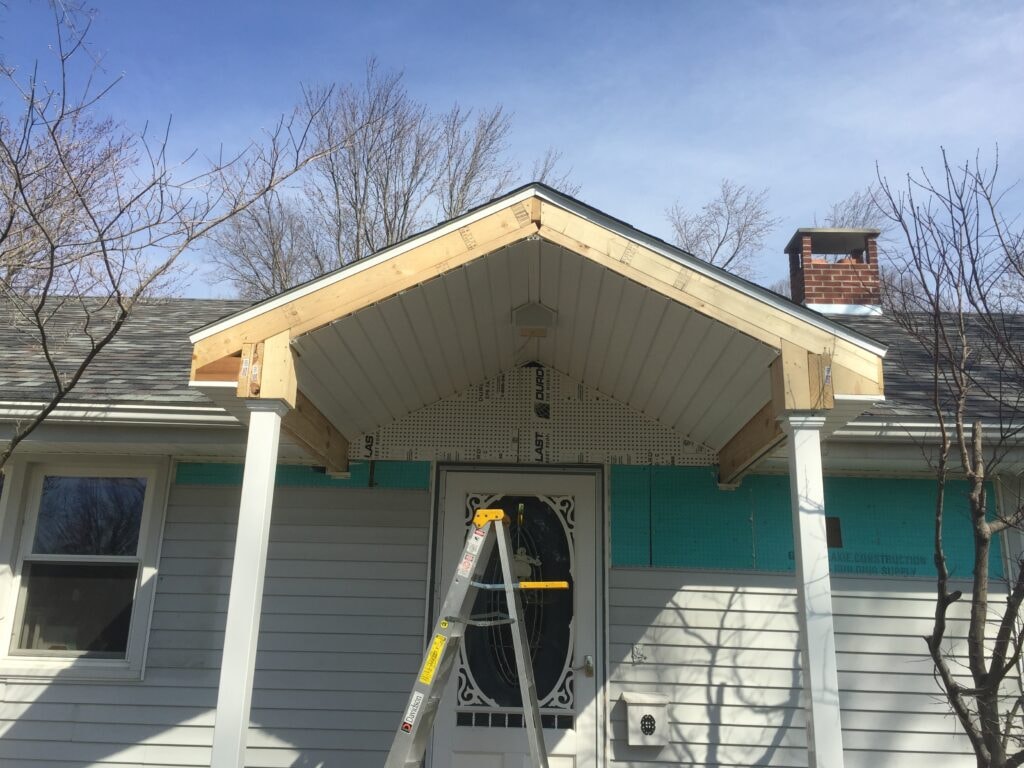 Front porch roof addition Findlay — during: gable roof framed and sheathed with white columns in place, close-up view, Findlay, Ohio