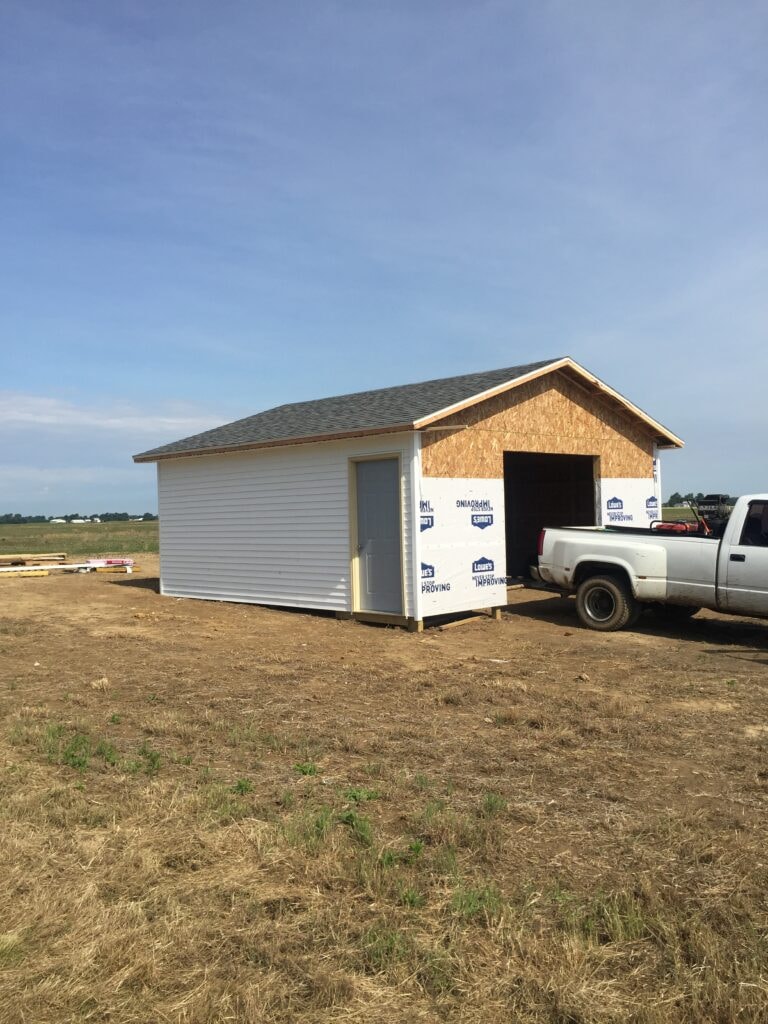 Garage build Arcadia — near complete: white vinyl siding partially installed with entry door hung and garage opening framed, Arcadia, Ohio