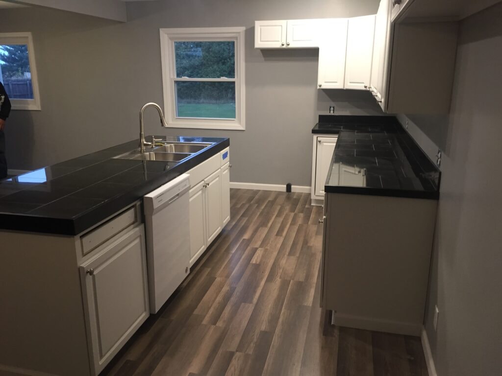 Kitchen family room remodel Arcadia — after: finished kitchen with white cabinets, black tile countertops, and new flooring, Arcadia, Ohio