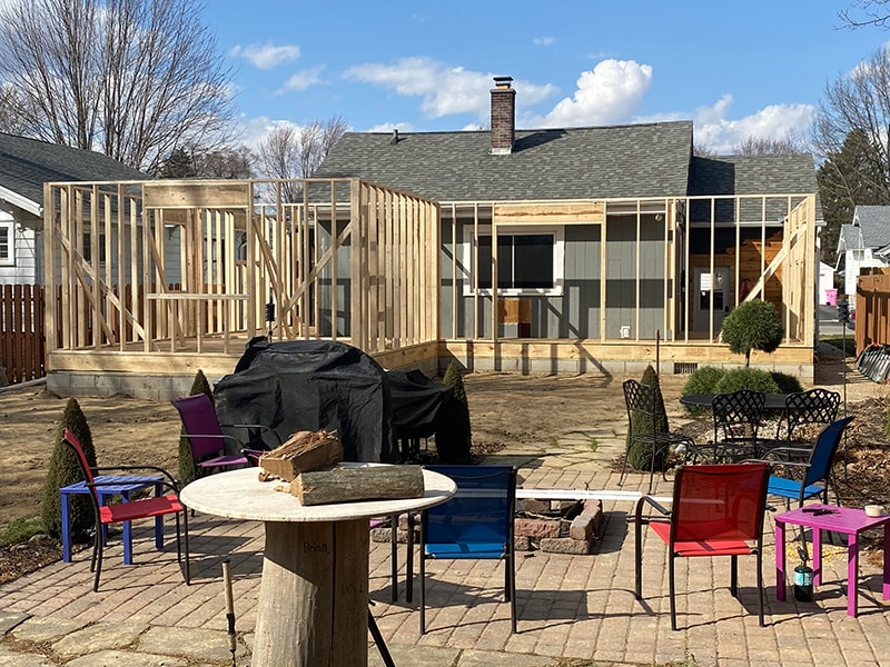 Large home addition — framing stage with full stud walls and window openings visible from backyard patio, Findlay, Ohio