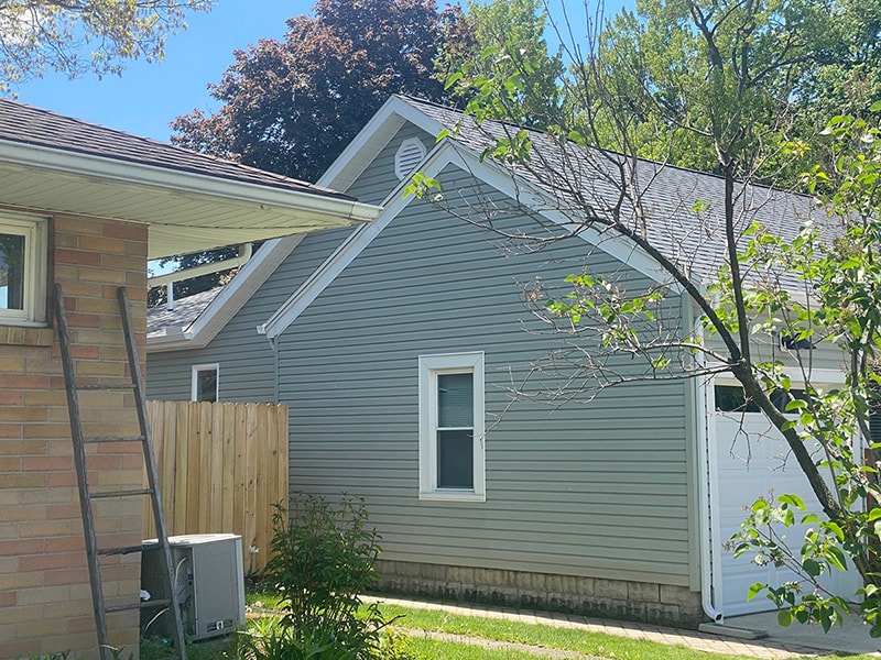 Large home addition — completed exterior front gable view with gray vinyl siding, round vent, and garage door, Findlay, Ohio