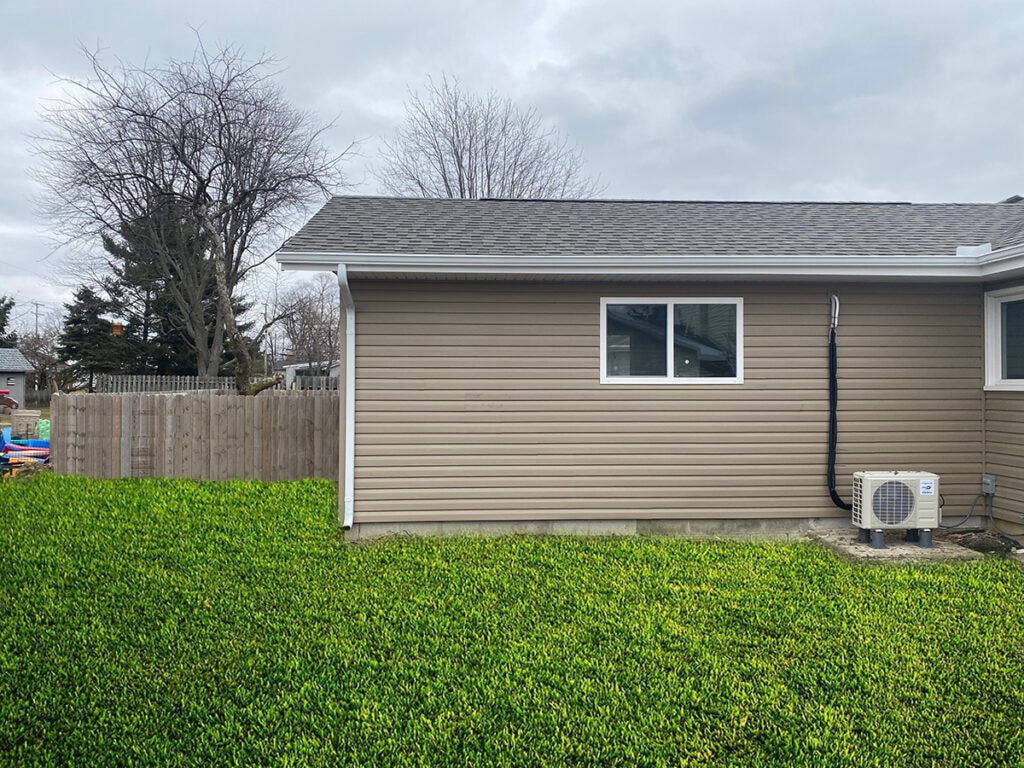 Large room addition Findlay — after: completed exterior rear wall with new tan vinyl siding, double-hung window, and mini-split condenser unit, Findlay, Ohio