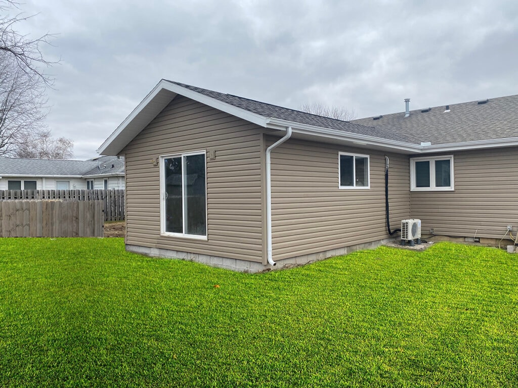 Large room addition Findlay — after: completed exterior wide angle showing gable roof, sliding glass door, double-hung window, gutters, and mini-split condenser, Findlay, Ohio