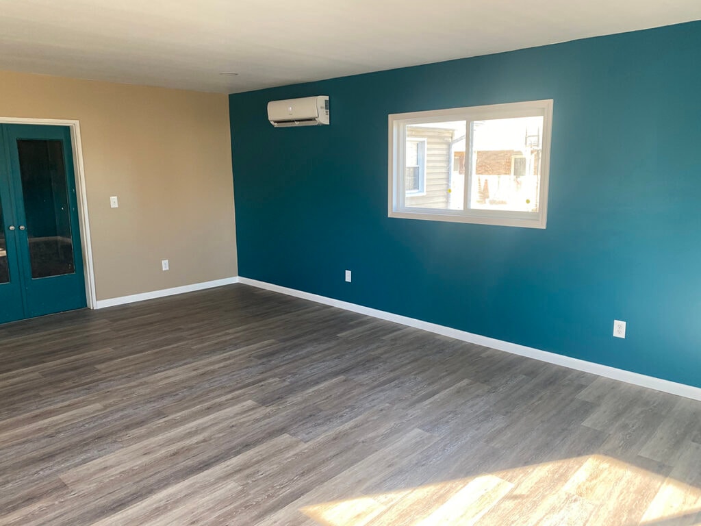 Large room addition Findlay — after: interior finished with teal accent wall, tan walls, gray LVP flooring, white trim, mini-split HVAC, and teal entry door, Findlay, Ohio