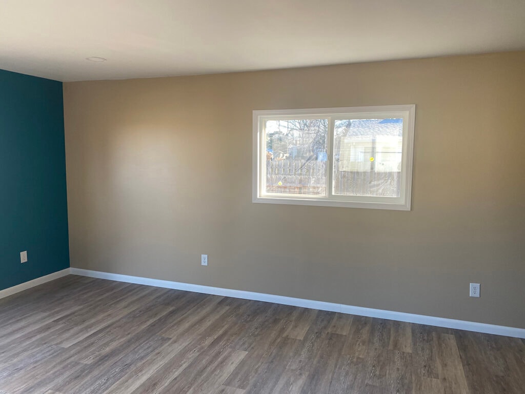 Large room addition Findlay — after: interior opposite wall showing tan paint, double-hung window, gray LVP flooring, white baseboards, and teal accent wall, Findlay, Ohio