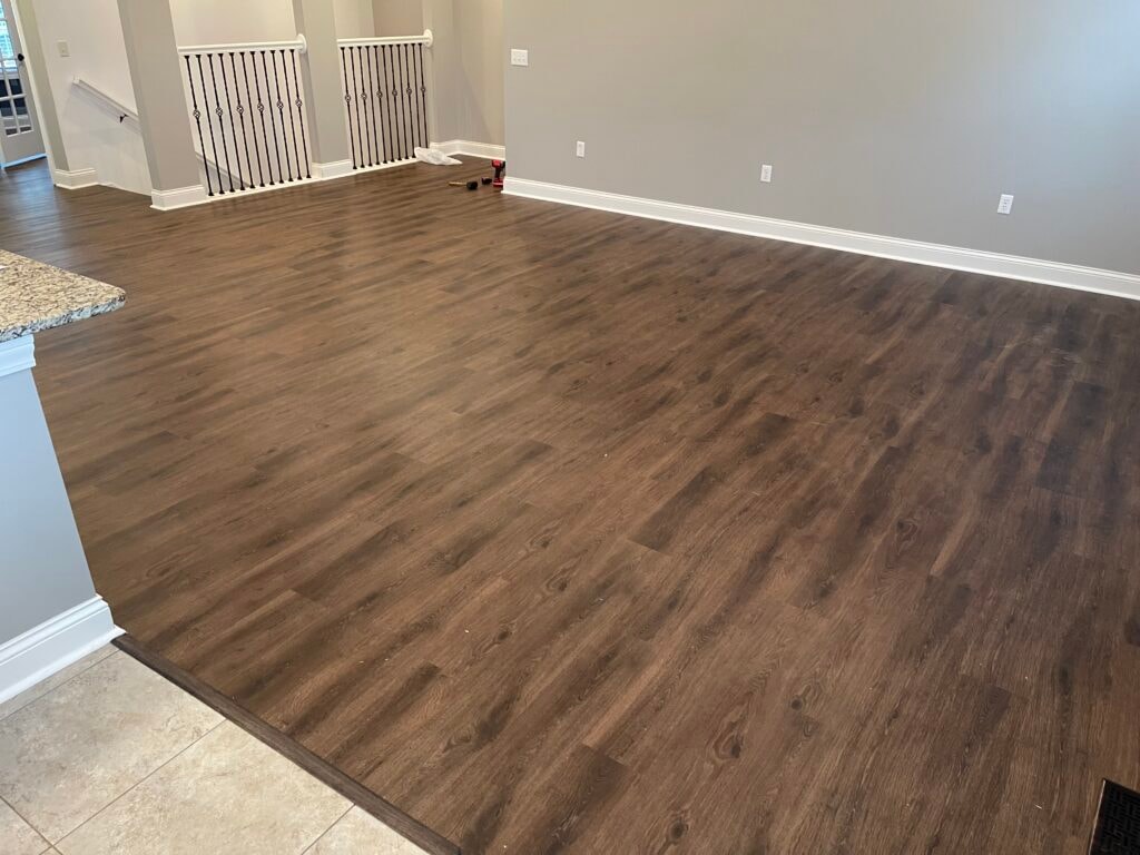 New LVP flooring — open living room with dark wood-look LVP, iron staircase railing, and granite kitchen counter, Findlay, Ohio