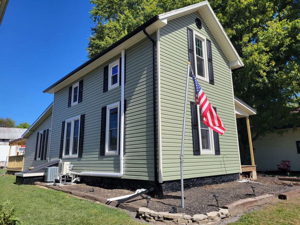 New siding and deck — after, side view with new sage green siding, white trim, black shutters, and American flag, Benton Ridge, Ohio