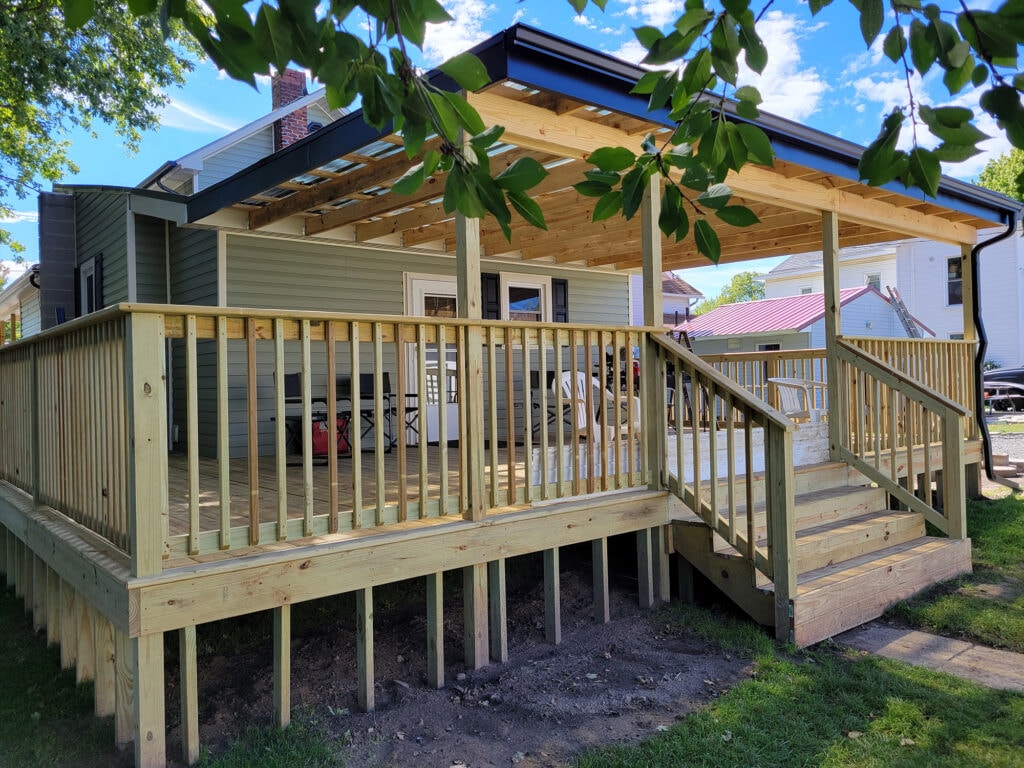 New siding and deck — after, completed back deck with pergola roof, full railing, and stairs from rear yard view, Benton Ridge, Ohio