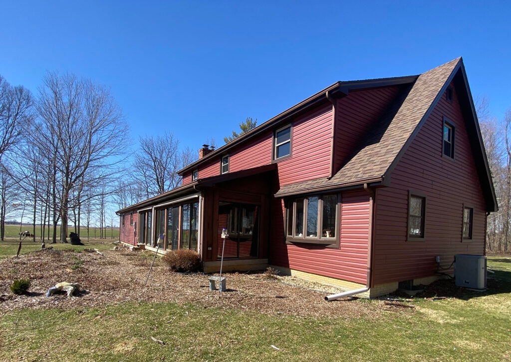 New siding Findlay — after: rear of home with new dark red vinyl siding and sunroom, open country views, Findlay, Ohio