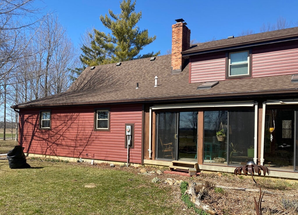 New siding Findlay — after: side rear of home with new dark red vinyl siding, sunroom, and open field views, Findlay, Ohio