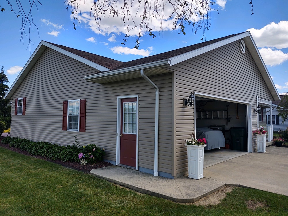 New siding Tiffin — after: garage side wide view with new tan vinyl siding, red shutters, open garage, and blue sky, Tiffin, Ohio