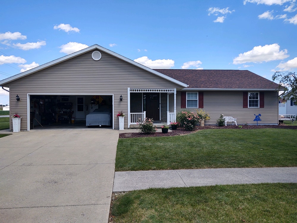 New siding Tiffin — after: full front view of home with new tan vinyl siding, red shutters, and white porch railing under blue sky, Tiffin, Ohio