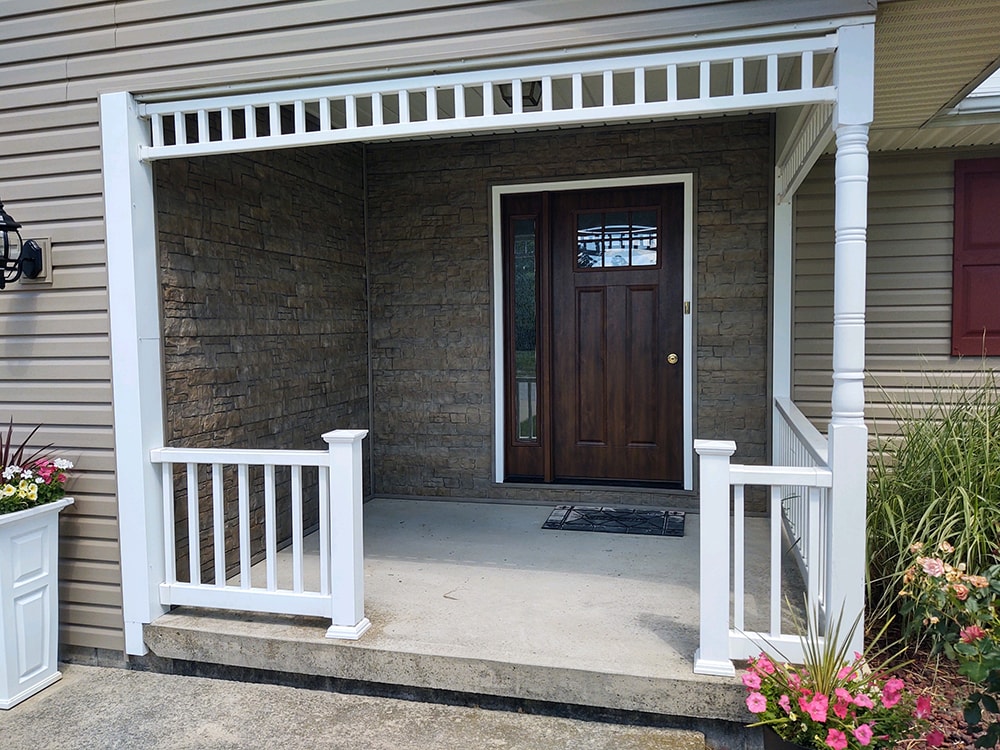 New siding Tiffin — after: front porch close-up with new stacked stone accent wall, white pergola railing, and dark wood front door, Tiffin, Ohio