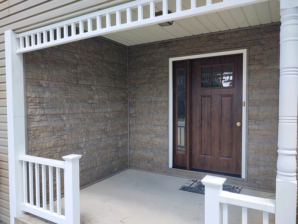 New siding Tiffin — after: front porch wide view with stacked stone walls, white columns and railing, and new dark wood entry door, Tiffin, Ohio