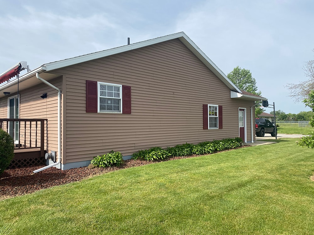 New siding Tiffin — after: side view of home with new tan vinyl siding, red shutters, and updated gutters, Tiffin, Ohio