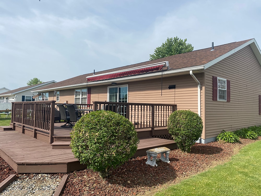 New siding Tiffin — after: rear of home with new tan vinyl siding, composite deck with dark railing, and retractable awning, Tiffin, Ohio