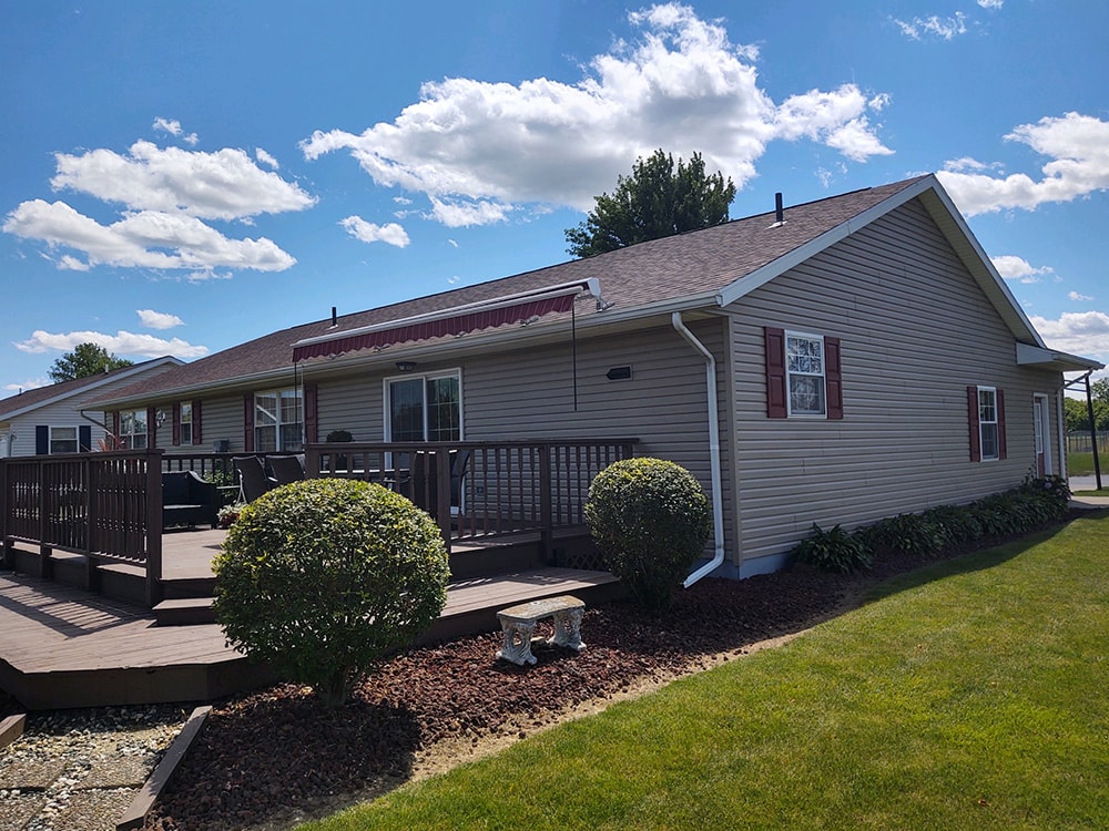 New siding Tiffin — after: rear wide view of home with new tan vinyl siding, composite deck, awning, and manicured landscaping, Tiffin, Ohio