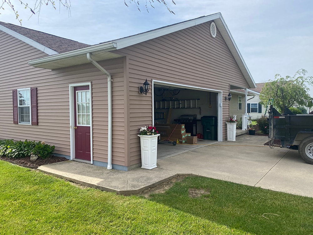 New siding Tiffin — after: garage side of home with new tan vinyl siding, red door, and open two-car garage, Tiffin, Ohio