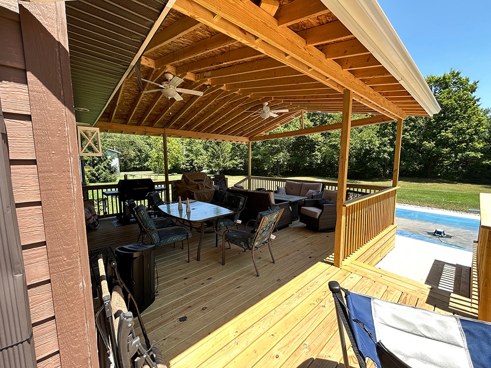 New treated deck with gable — interior view under gable roof with ceiling fans, dining set, and pool