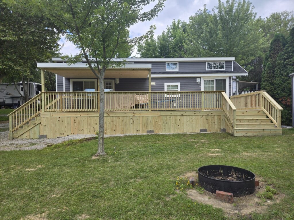 New treated deck with roof — completed full front view with dual staircase and partial roof — campground