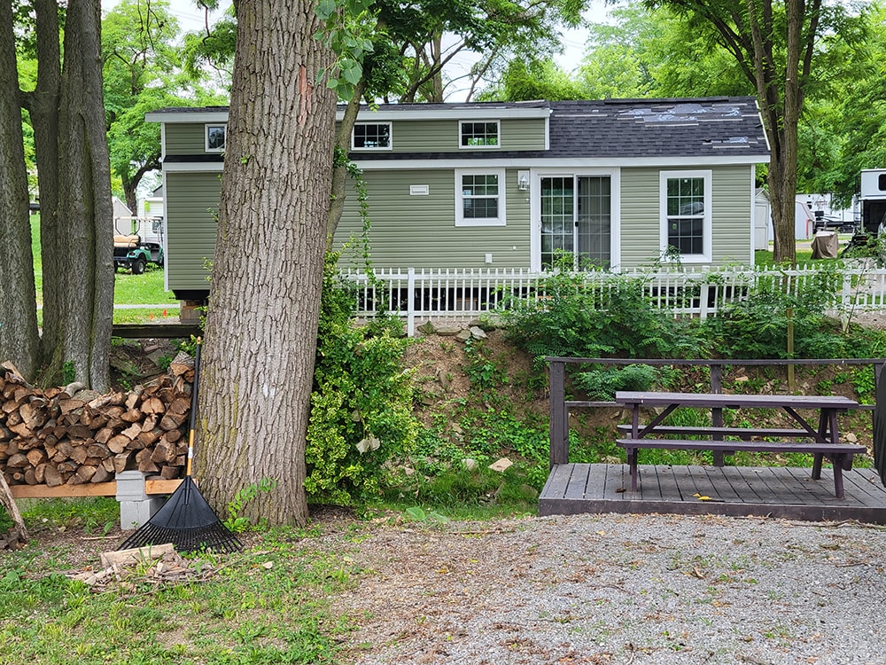 New treated deck — green park model exterior view with white picket fence and wooded surroundings — Wapakoneta campground