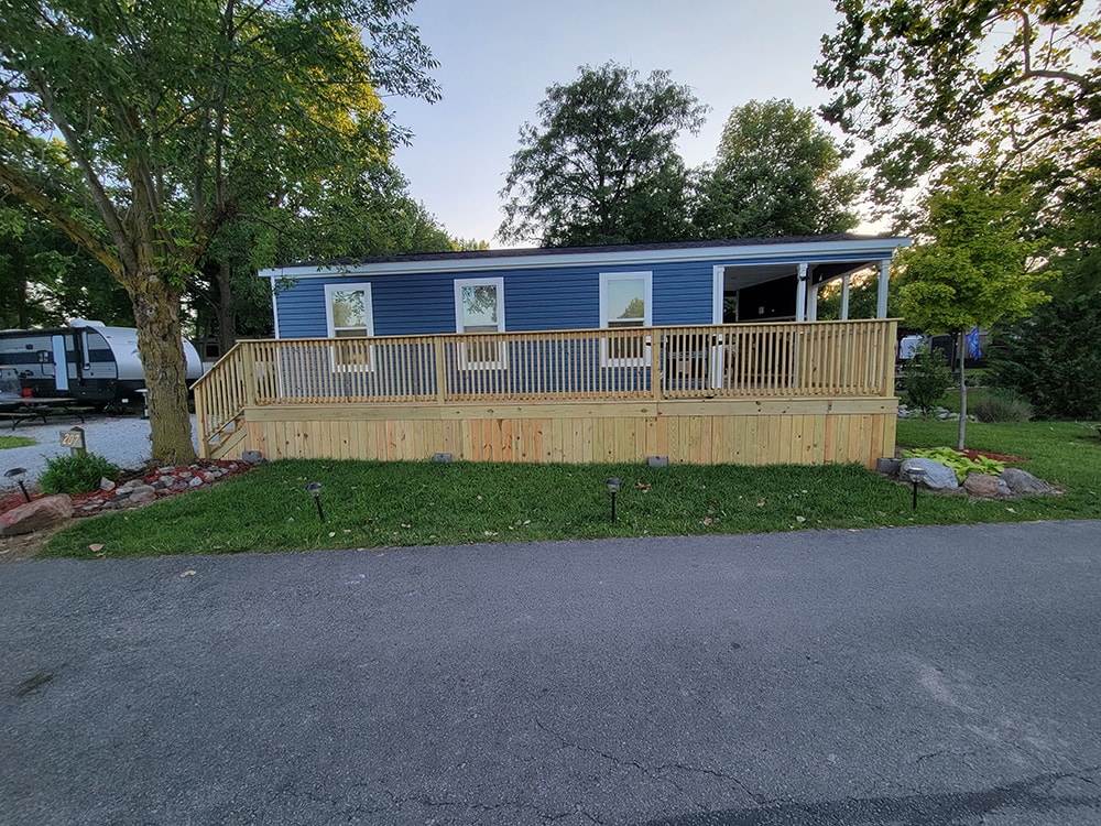 New treated deck — after: blue park model with completed full-width treated wood deck and railing — Wapakoneta campground