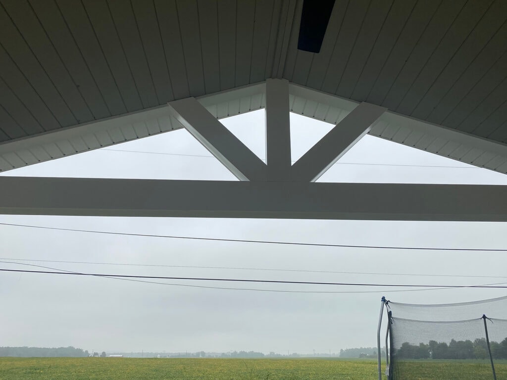 Patio addition Fostoria — after: close-up looking up at white painted gable truss with decorative knee braces and tongue-and-groove beadboard ceiling under overcast sky, Fostoria, Ohio