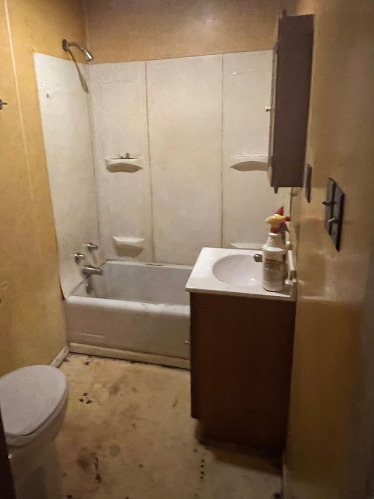 Rental home remodel before — bathroom with old tub surround, dated vanity, and worn flooring, Findlay, Ohio