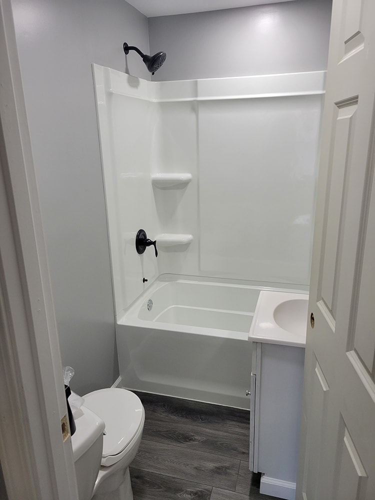 Rental home remodel after — bathroom with new tub, shower surround, toilet, and luxury vinyl plank flooring, Findlay, Ohio