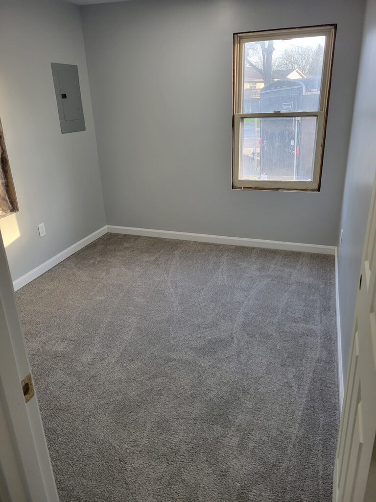 Rental home remodel after — bedroom with fresh gray paint, new carpet, and electrical panel, Findlay, Ohio