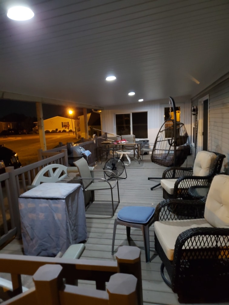 Roof addition existing deck Findlay — after: night shot of full covered deck lit by recessed ceiling lights with egg chair, wicker seating, covered grill, and neighborhood glowing in background, Findlay, Ohio