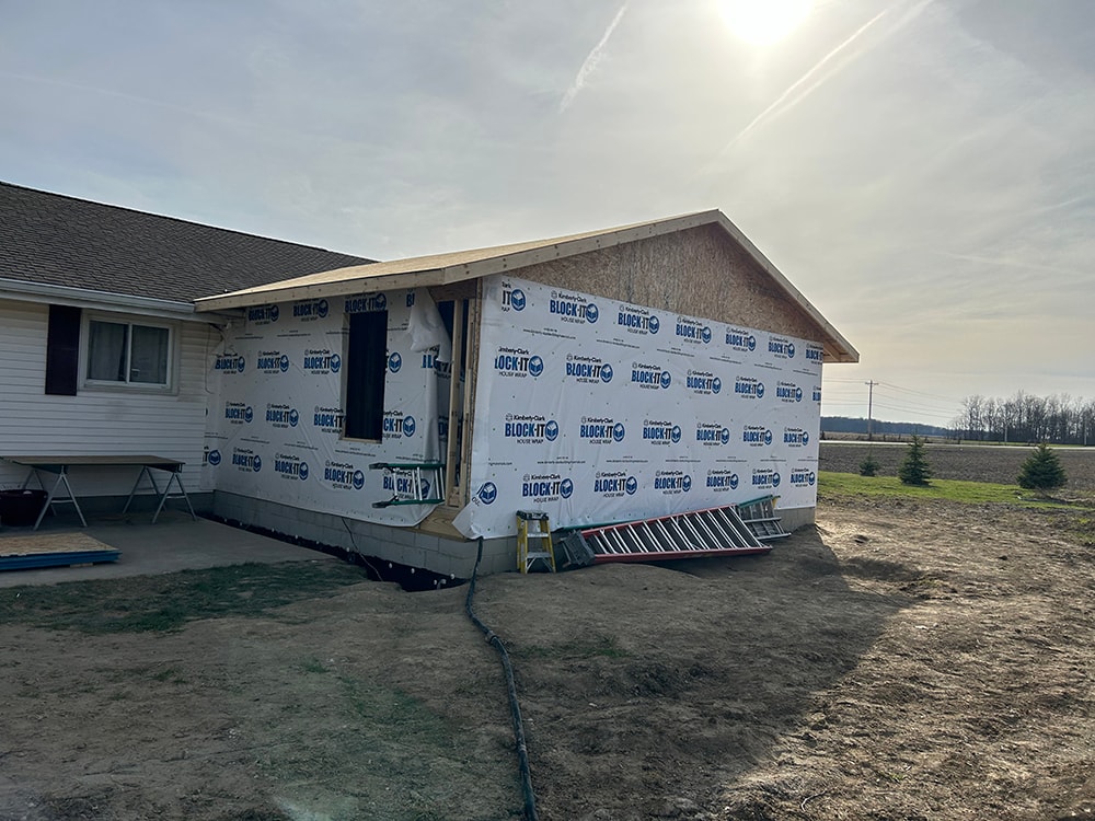 Home addition — framing stage with house wrap and ladder against exterior — Findlay, Ohio