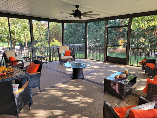 Screened-in composite deck — after: interior view with ceiling fan, composite decking, and orange accent furniture — Findlay, Ohio