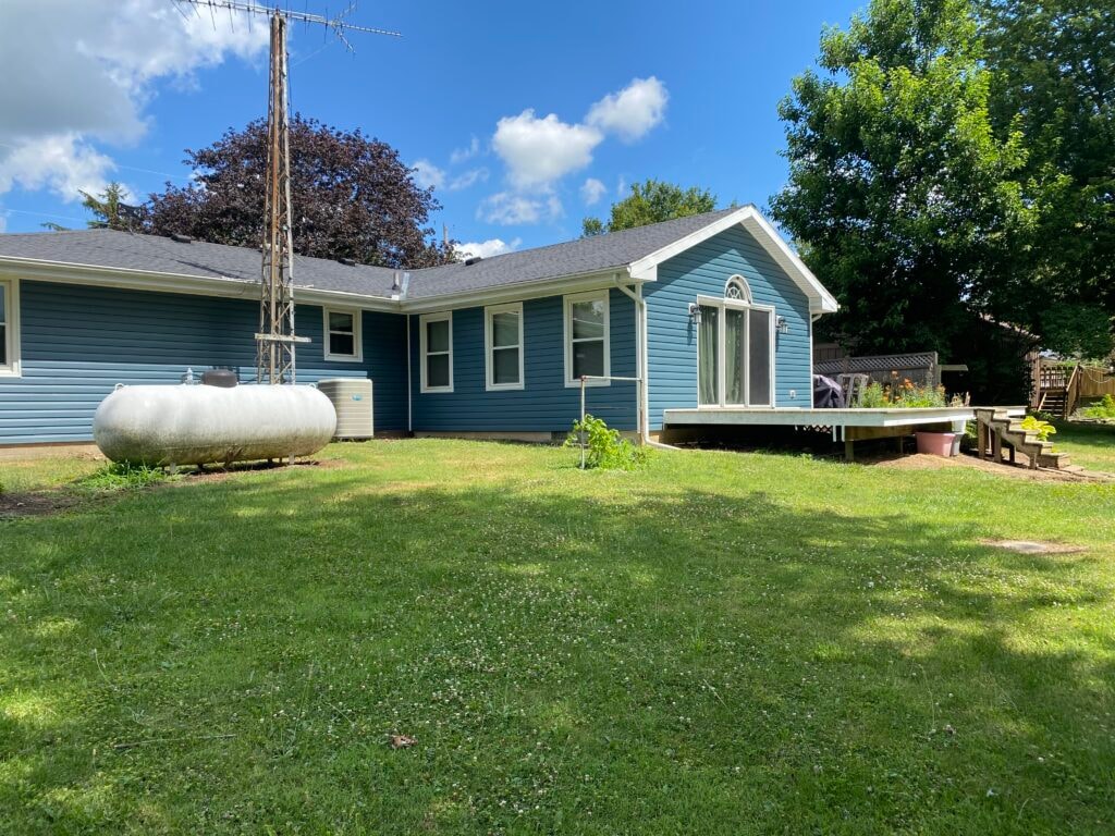 Siding job Findlay — after: rear of home with completed blue vinyl siding, white trim, existing deck with steps, propane tank, and TV antenna, Findlay, Ohio