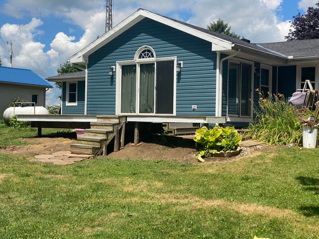Siding job Findlay — after: rear close-up of new blue vinyl siding on addition bump-out with arched window, deck stairs, and garden plantings, Findlay, Ohio